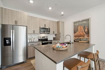 a kitchen with stainless steel appliances and a large island with bar stools at The Maddox Luxury Apartment Homes, Arizona